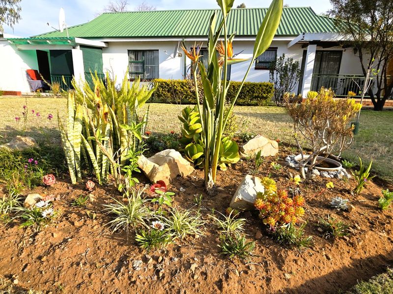 A view of the rear exterior of the townhouse featuring a well-maintained garden bed, lawn, and white facade with green metal roofing.