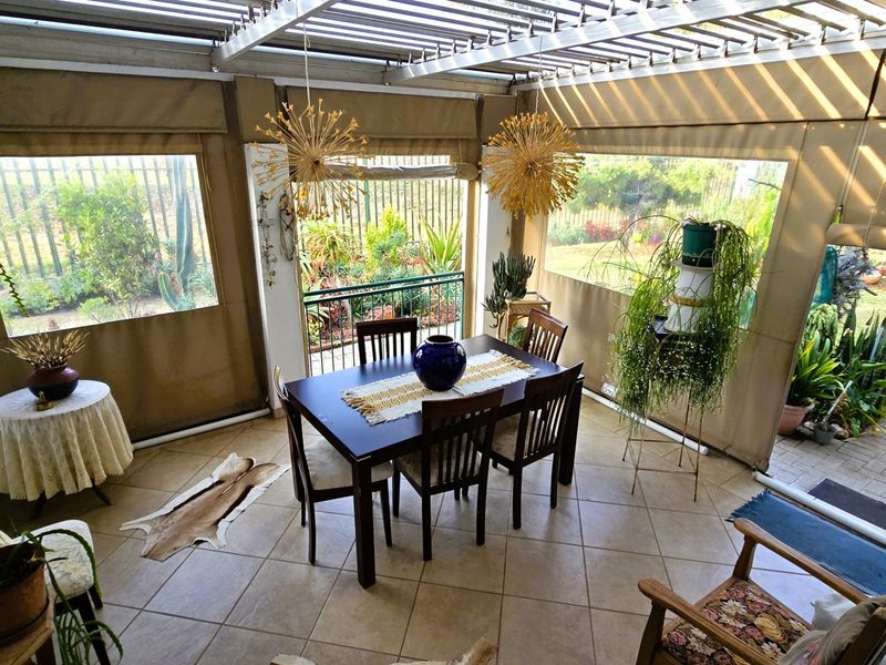 A covered patio area featuring a slatted roof, durable tiled flooring, and roll-up canvas blinds, providing a versatile outdoor dining space overlooking the garden.