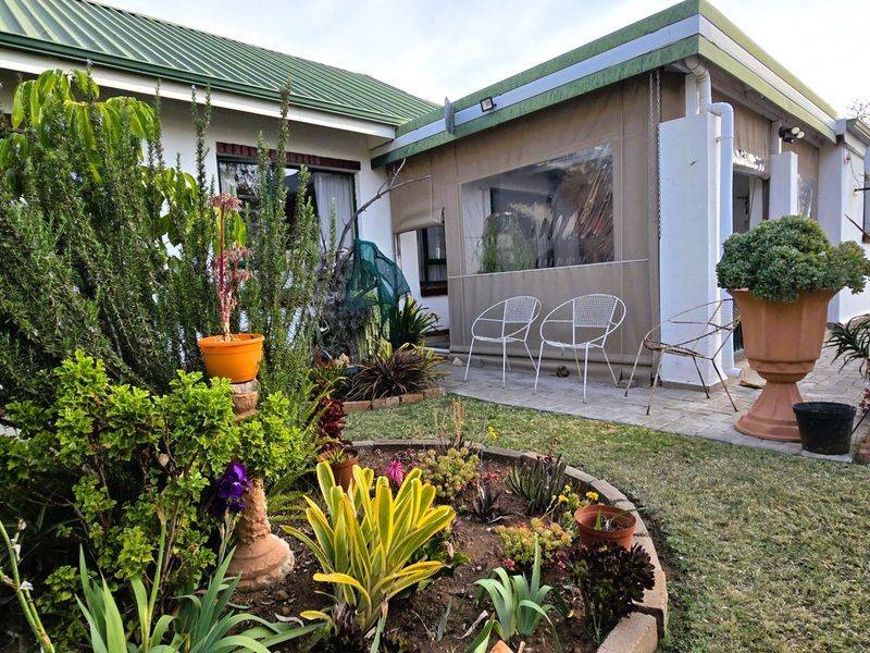 A rear exterior view of the townhouse featuring a paved patio area with a canvas enclosure and a landscaped garden with established plants.