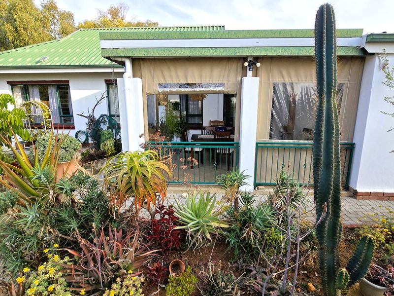 A covered patio area featuring paved flooring, metal balustrades, and protective canvas blinds, overlooking a well-established garden.