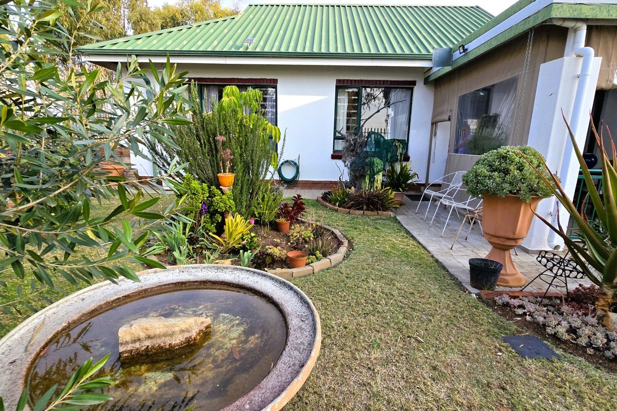 A well-maintained rear garden featuring a paved patio area, established landscaping, and a central water feature, adjacent to the townhouse structure.