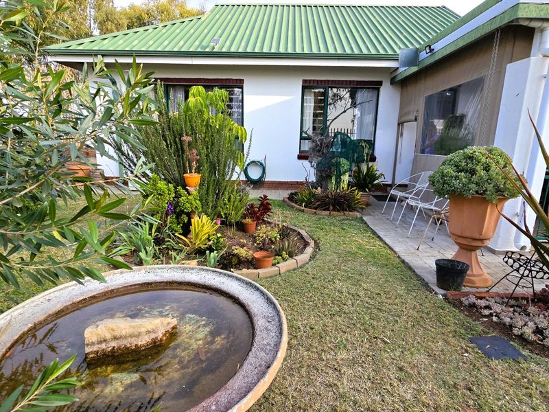 A well-maintained rear garden featuring a paved patio area, established landscaping, and a central water feature, adjacent to the townhouse structure.