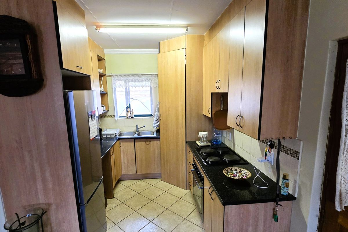 A functional galley-style kitchen featuring laminate cabinetry, dark countertops, a built-in oven, electric hob, and tiled flooring.