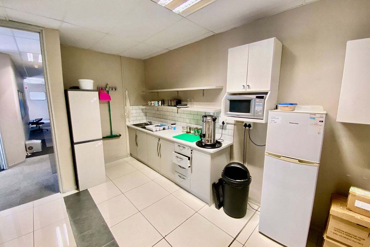 A functional commercial kitchenette featuring built-in cabinetry, subway tile backsplash, stainless steel sink, and integrated microwave, with tiled flooring throughout.