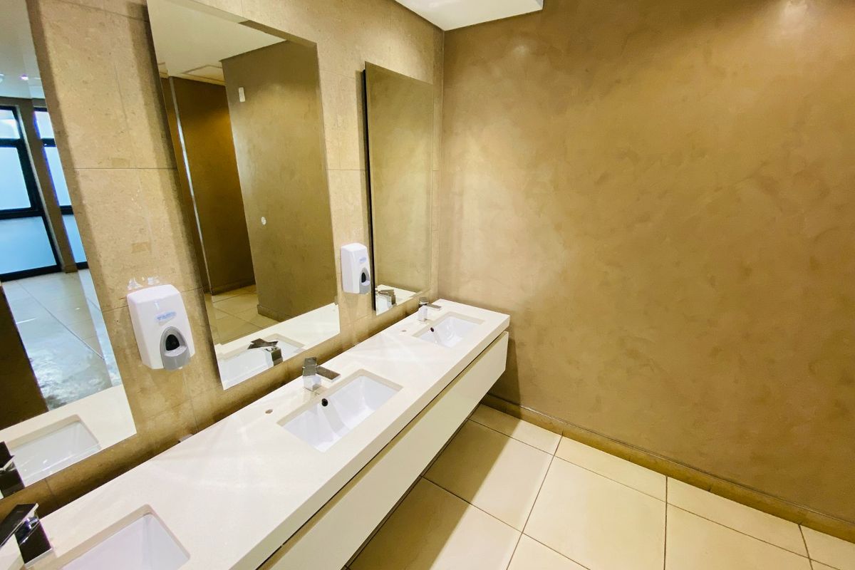 Modern commercial bathroom featuring a double vanity with integrated sinks, large wall mirrors, and neutral tiled finishes.