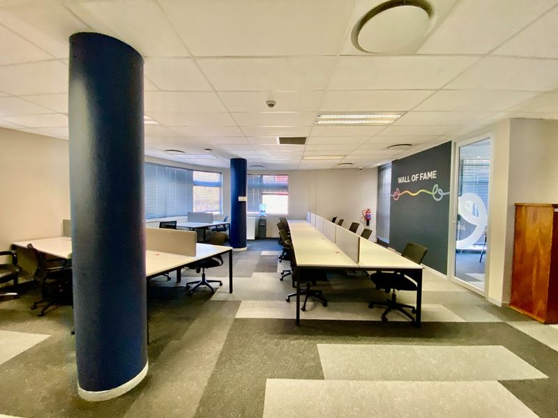 Open-plan commercial office space featuring carpeted flooring, suspended ceilings with recessed lighting, and large windows with venetian blinds.