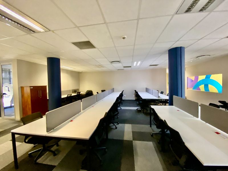 Open-plan commercial office space featuring rows of built-in workstations, suspended ceilings, and carpeted flooring.