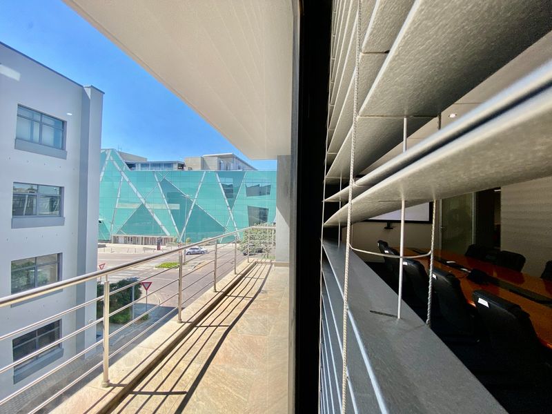 A modern balcony featuring stone tile flooring and a stainless steel balustrade, offering an elevated view of the surrounding commercial office buildings.