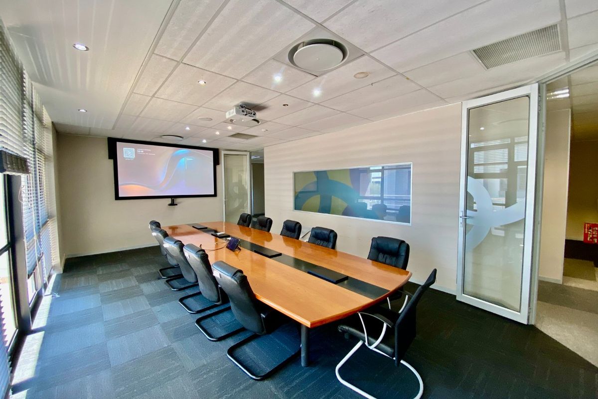 A professional boardroom featuring a large conference table, integrated projector system, suspended ceiling, and glass partition walls for a modern commercial workspace.