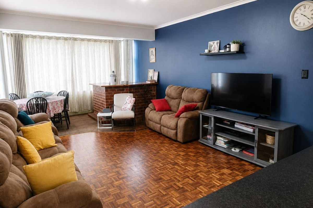 Open plan living and dining area featuring classic parquet flooring, a brick breakfast bar, and a bold blue feature wall.