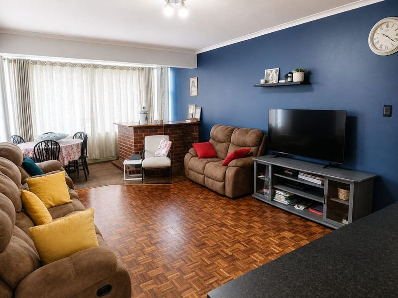 Open plan living and dining area featuring classic parquet flooring, a brick breakfast bar, and a bold blue feature wall.