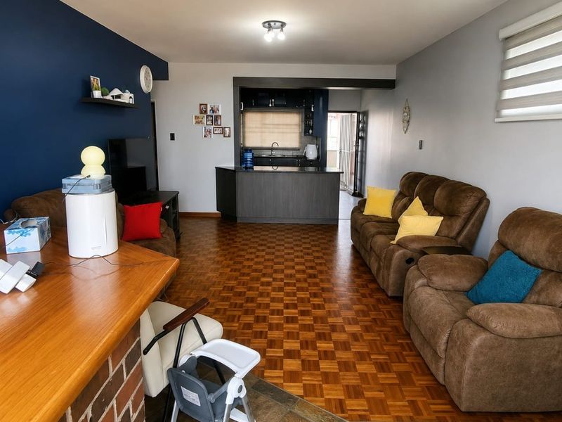 Open plan living area featuring parquet flooring, a brick breakfast bar, and a functional kitchen with dark cabinetry and a central island.