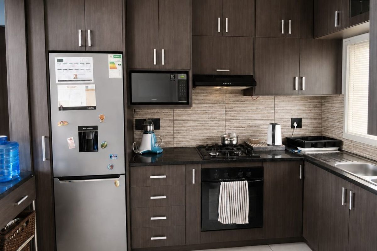 Modern kitchen featuring dark wood cabinetry, stone countertops, built-in oven, gas hob, and integrated microwave with neutral tiled flooring.