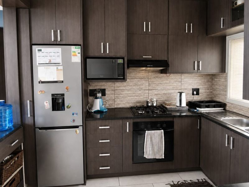 Modern kitchen featuring dark wood cabinetry, stone countertops, built-in oven, gas hob, and integrated microwave with neutral tiled flooring.