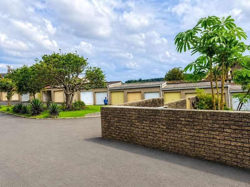 A view of a residential complex featuring a row of garages, a brick boundary wall, and well-maintained landscaped garden areas.