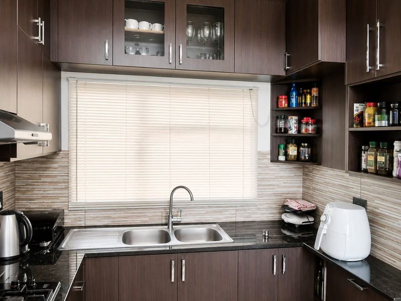 A well-maintained kitchen featuring dark wood cabinetry, granite countertops, a double stainless steel sink, and a gas hob with an integrated extractor fan.