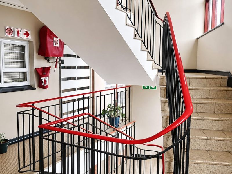 A functional stairwell featuring tiled steps, a red and black metal balustrade, and integrated fire safety equipment.