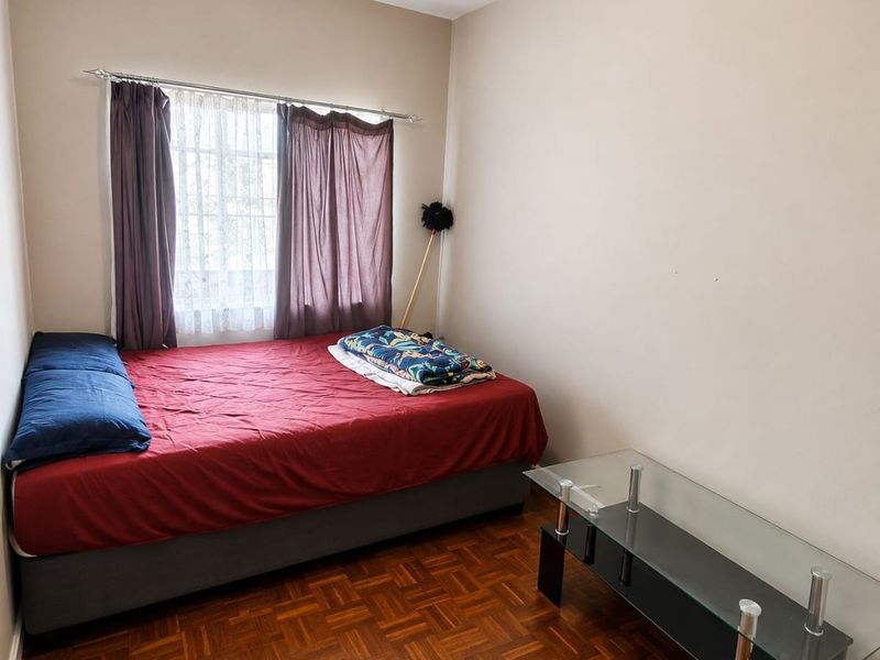 A bedroom featuring classic parquet flooring and a window with a curtain rod, providing a neutral space ready for personalization.