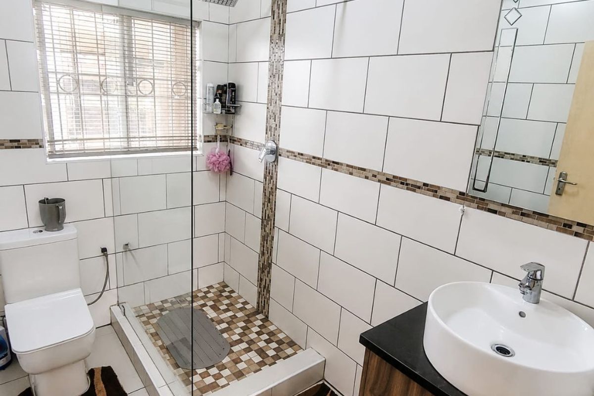 Modern bathroom featuring a glass-enclosed walk-in shower, vessel sink vanity, and contemporary white wall tiling with decorative mosaic accents.