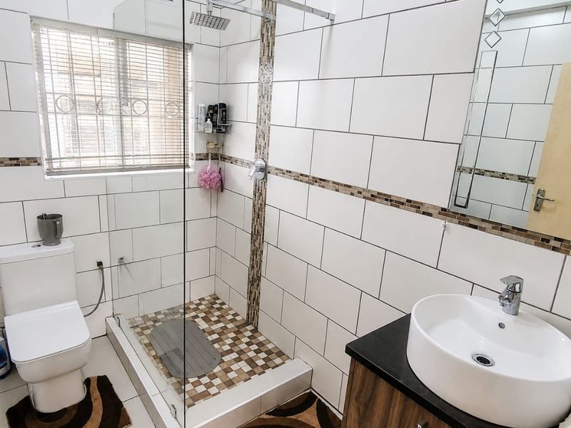 Modern bathroom featuring a glass-enclosed walk-in shower, vessel sink vanity, and contemporary white wall tiling with decorative mosaic accents.