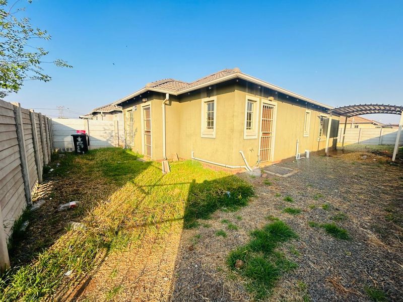 Rear view of the property featuring a tiled roof, security gates, a carport, and a large backyard area enclosed by a precast concrete wall.