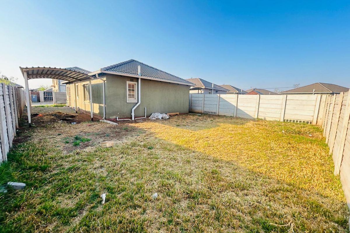 Rear view of the property featuring a tiled roof, carport, and a large backyard enclosed by precast concrete boundary walls.
