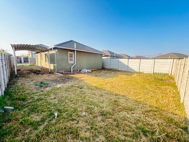 Rear view of the property featuring a tiled roof, carport, and a large backyard enclosed by precast concrete boundary walls.