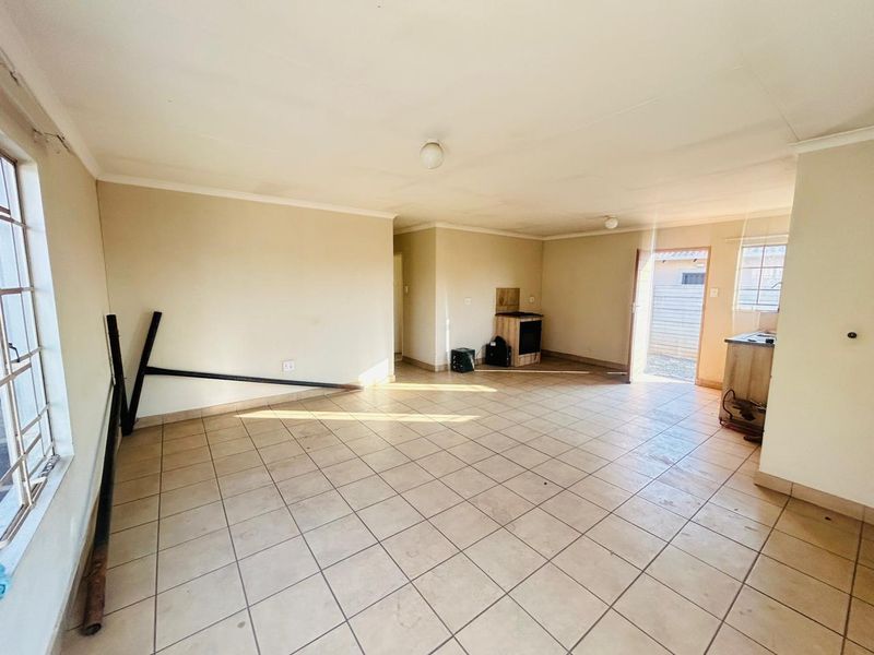 Spacious open-plan living and kitchen area featuring tiled flooring, security bars on windows, and basic built-in kitchen cabinetry.