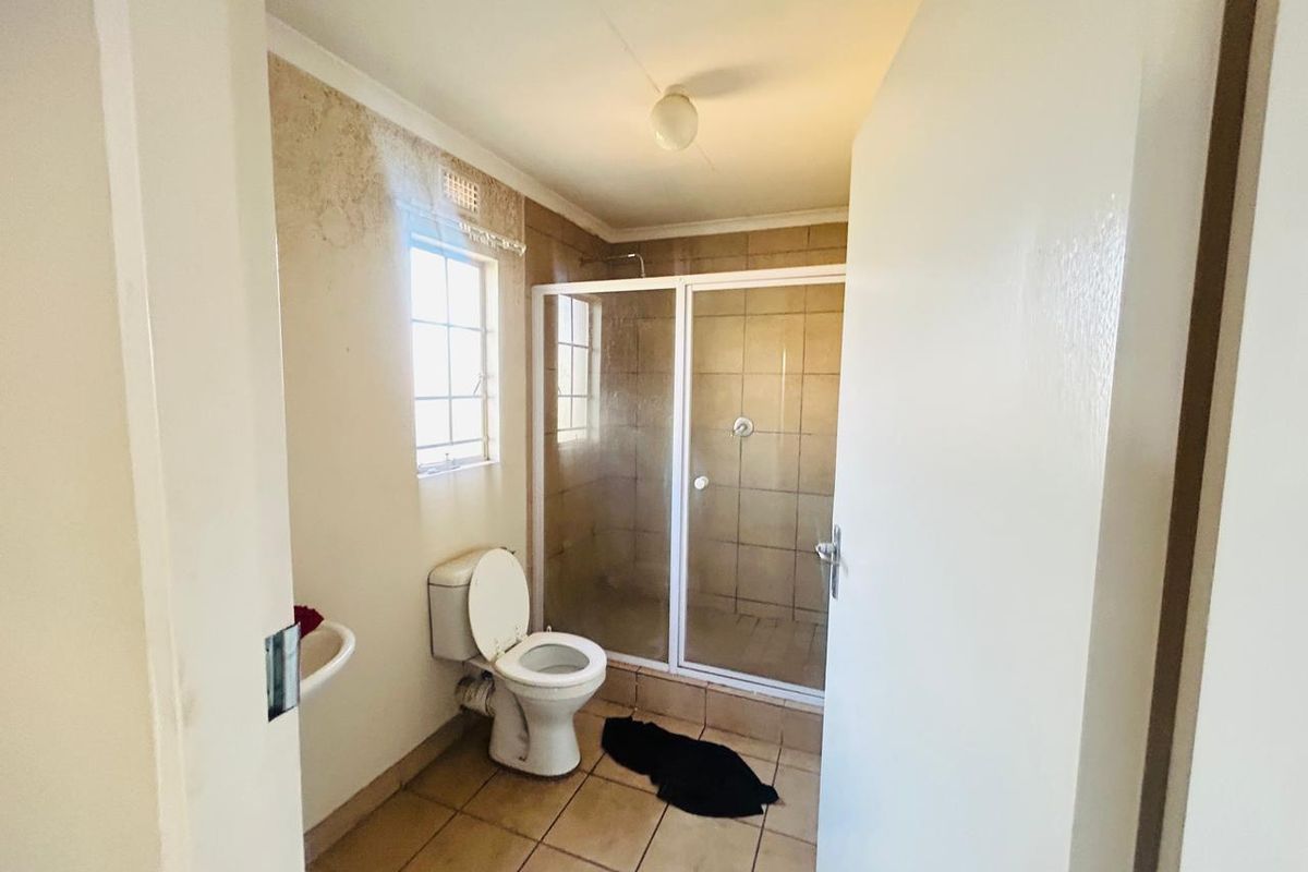 A functional bathroom featuring a shower enclosure, toilet, and washbasin, currently showing signs of wall surface deterioration requiring maintenance.