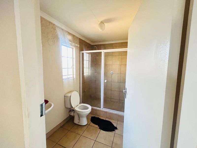 A functional bathroom featuring a shower enclosure, toilet, and washbasin, currently showing signs of wall surface deterioration requiring maintenance.