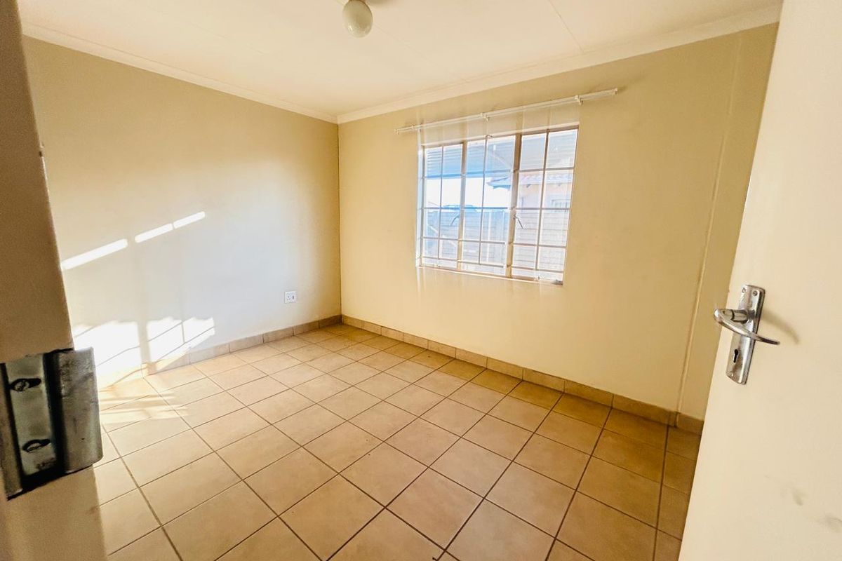 An empty bedroom featuring tiled flooring, neutral walls, and a window fitted with security bars.