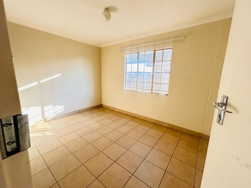 An empty bedroom featuring tiled flooring, neutral walls, and a window fitted with security bars.