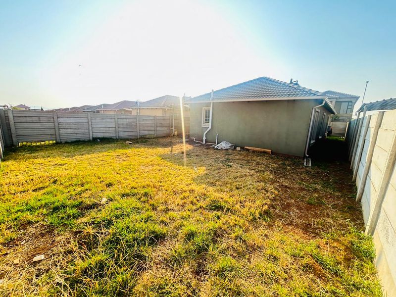 A view of the rear exterior of the property featuring a tiled roof, external plumbing, and a fenced backyard area.