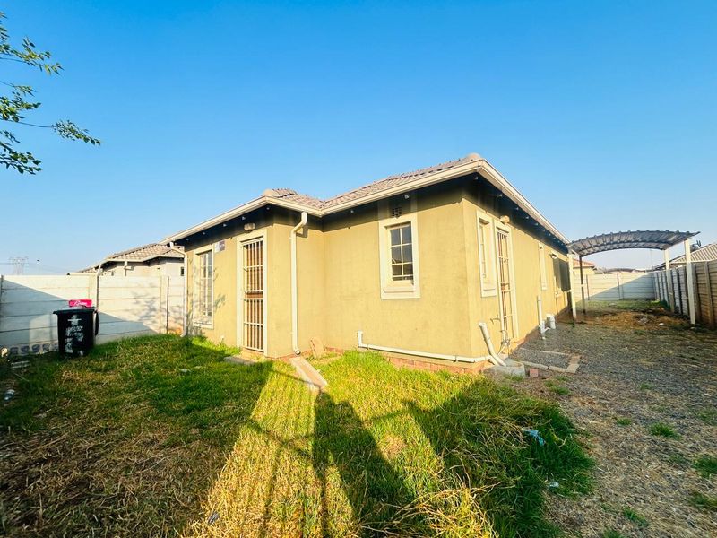 Rear view of the property featuring a tiled roof, security gates, and a precast concrete boundary wall with an adjacent carport structure.