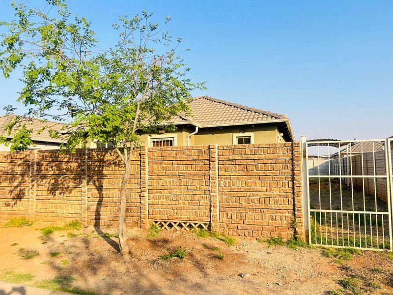 A view of the rear exterior featuring a brick boundary wall, metal gate, and a tiled roof house structure.