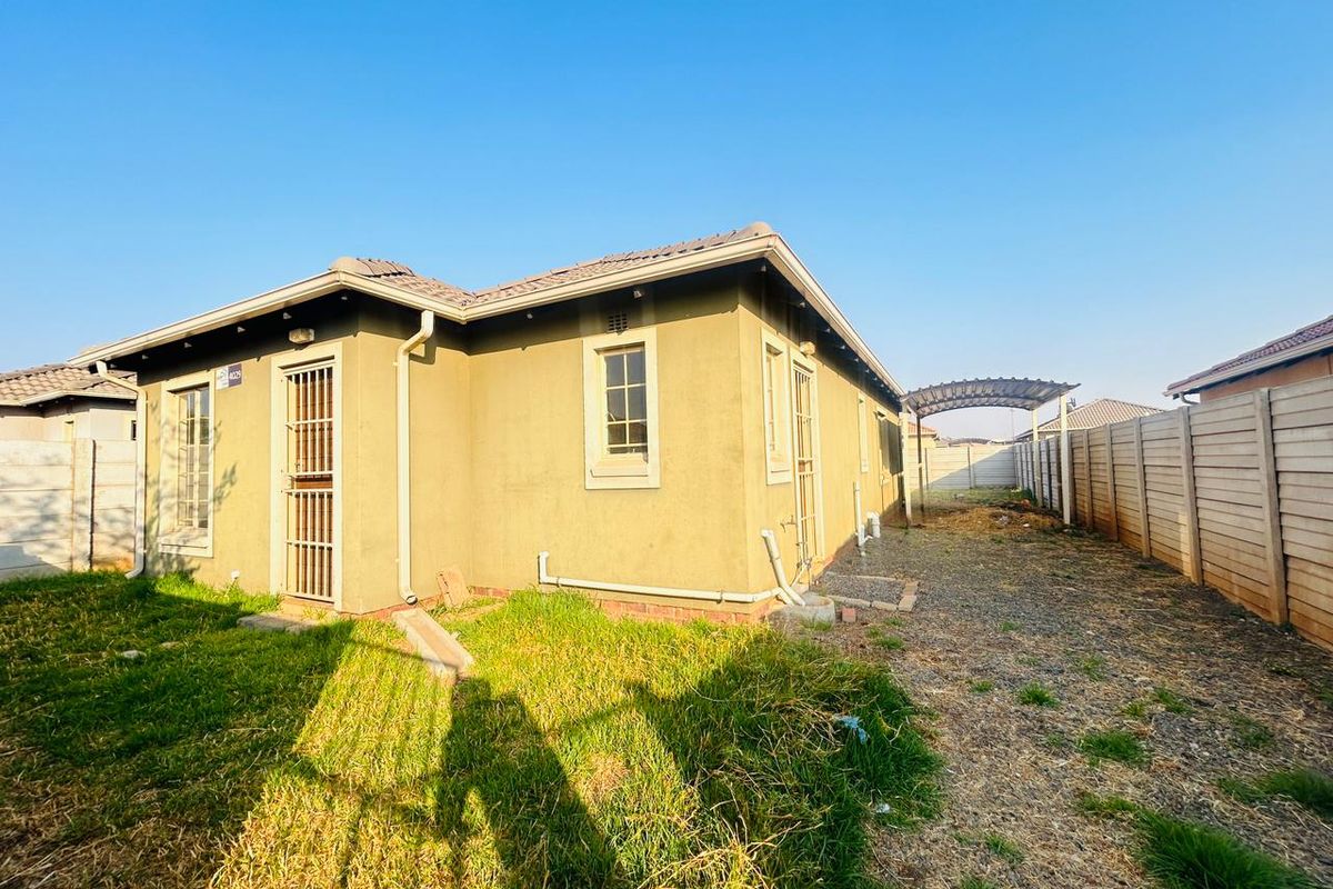 Rear view of the property featuring a tiled roof, security gates, and a spacious yard enclosed by precast concrete boundary walls.