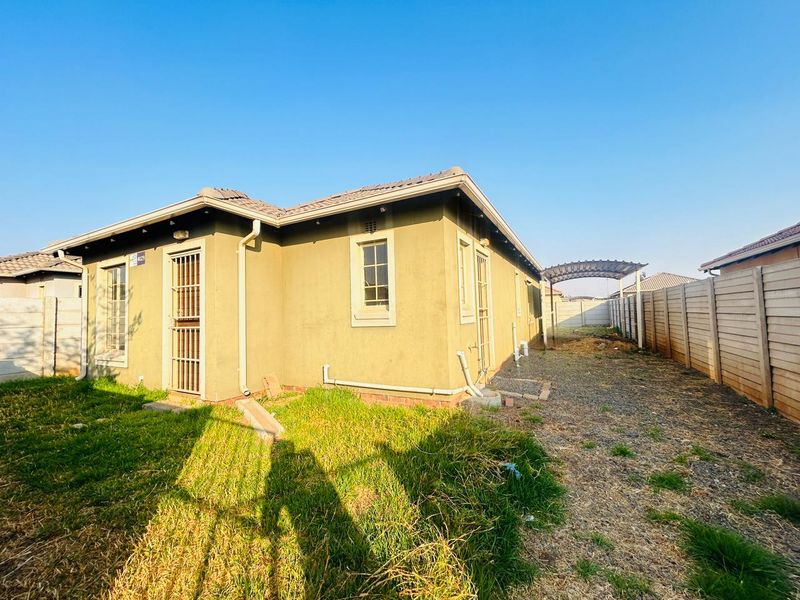 Rear view of the property featuring a tiled roof, security gates, and a spacious yard enclosed by precast concrete boundary walls.
