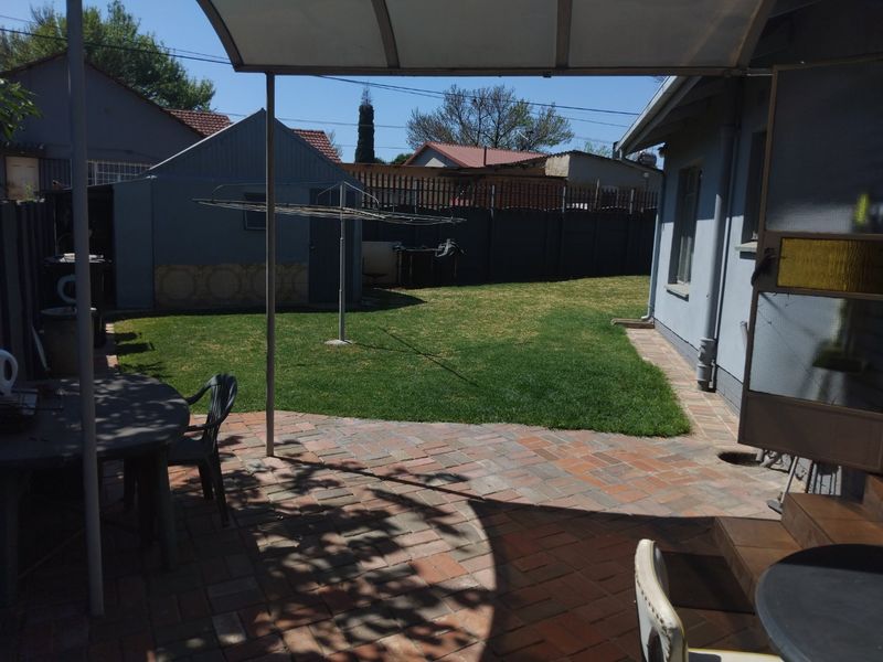 A covered brick-paved patio area overlooking a private backyard with a lawn and a detached outbuilding.