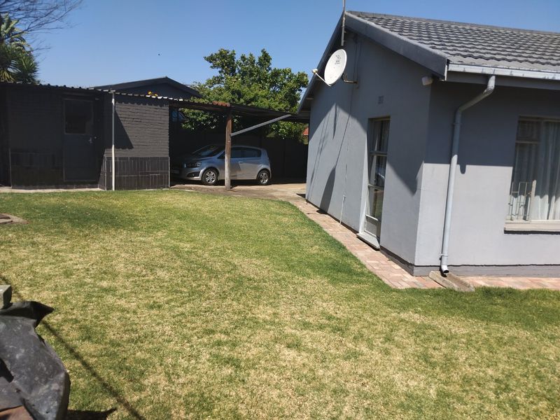 Rear view of the property featuring a lawn, paved walkway, and a covered carport area.