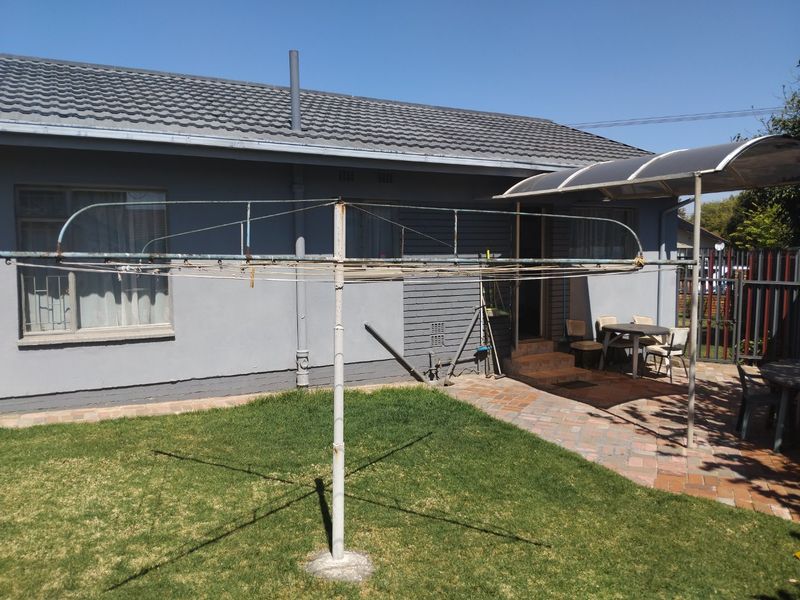 Rear exterior view of the house featuring a paved patio area, a covered outdoor space, and a rotary clothesline in the garden.
