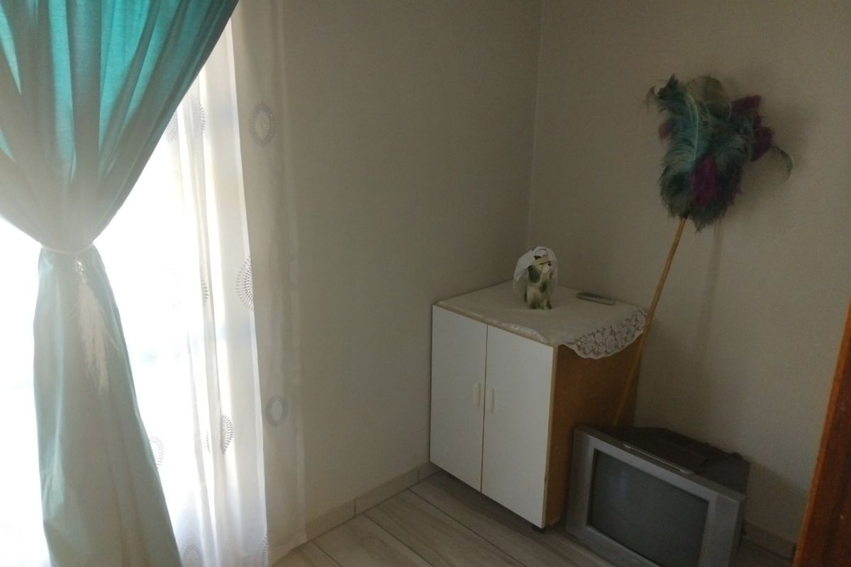 A simple bedroom space featuring tiled flooring and a window with curtains, providing a functional area for rest.