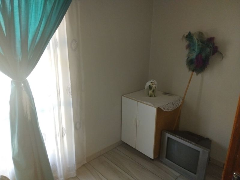 A simple bedroom space featuring tiled flooring and a window with curtains, providing a functional area for rest.