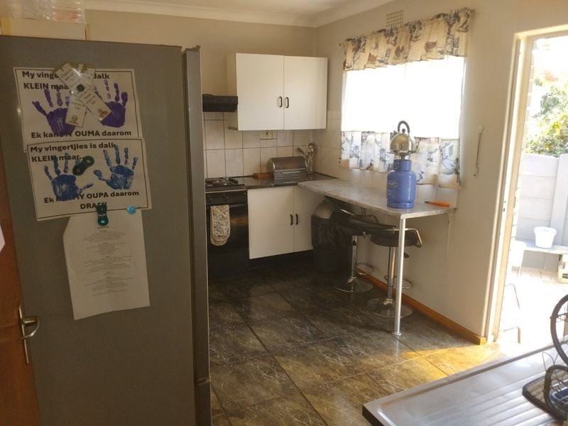A functional kitchen featuring built-in cabinetry, tiled flooring, a breakfast counter, and integrated cooking appliances with direct access to the exterior.