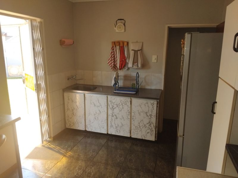 A functional scullery area featuring a stainless steel sink, tiled splashback, and built-in cabinetry with direct access to the exterior.