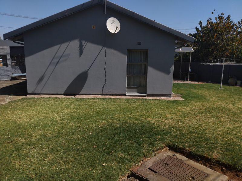 Rear view of the property featuring a grey exterior wall, a single door, a satellite dish, and a well-maintained lawn area.