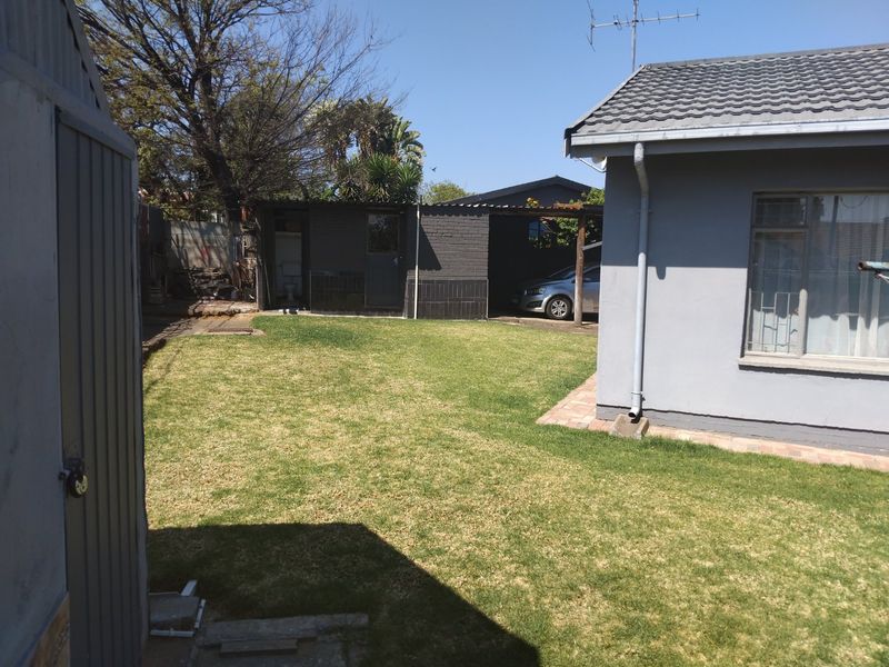 Rear garden view featuring a lawn, brick paving, and an outbuilding with an attached carport.