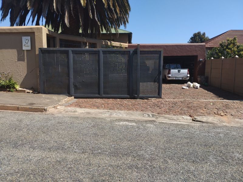 Front exterior view of the property featuring a modern metal sliding gate, a cobblestone driveway, and a covered carport area.