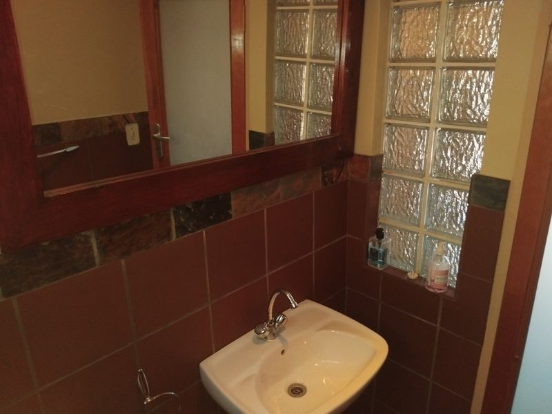 A compact bathroom featuring a wall-mounted basin, tiled splashback, and a distinctive glass block window for natural light.