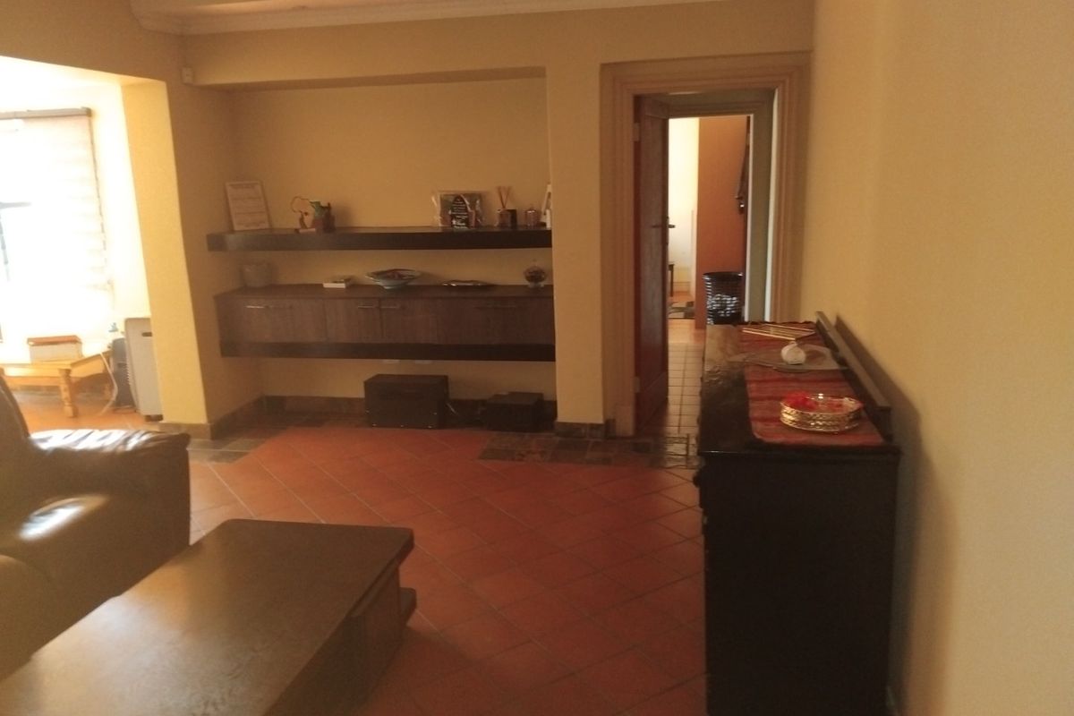A living room featuring terracotta floor tiles, built-in wall cabinetry with shelving, and recessed ceiling lighting, providing a functional and traditional living space.