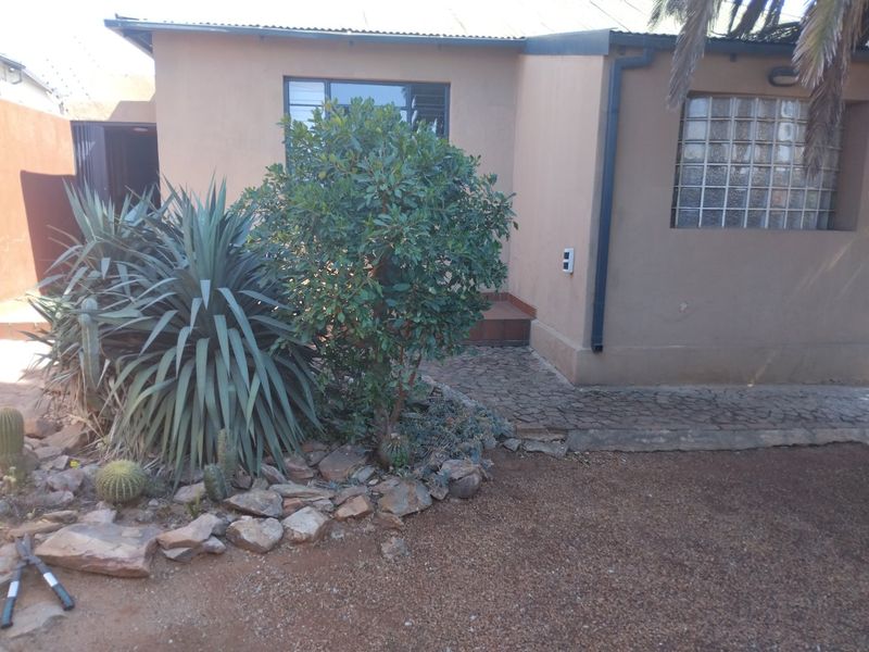 Front exterior view of the property featuring a paved walkway, glass block window, and established garden landscaping.
